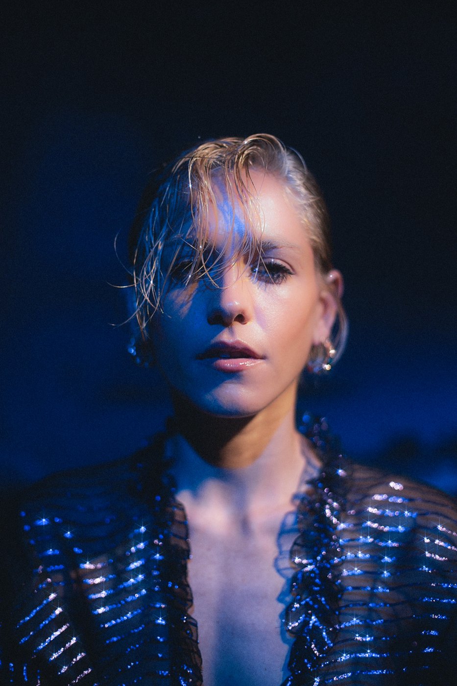 Close portrait with wet hair and sequined sheer jacket in blue light