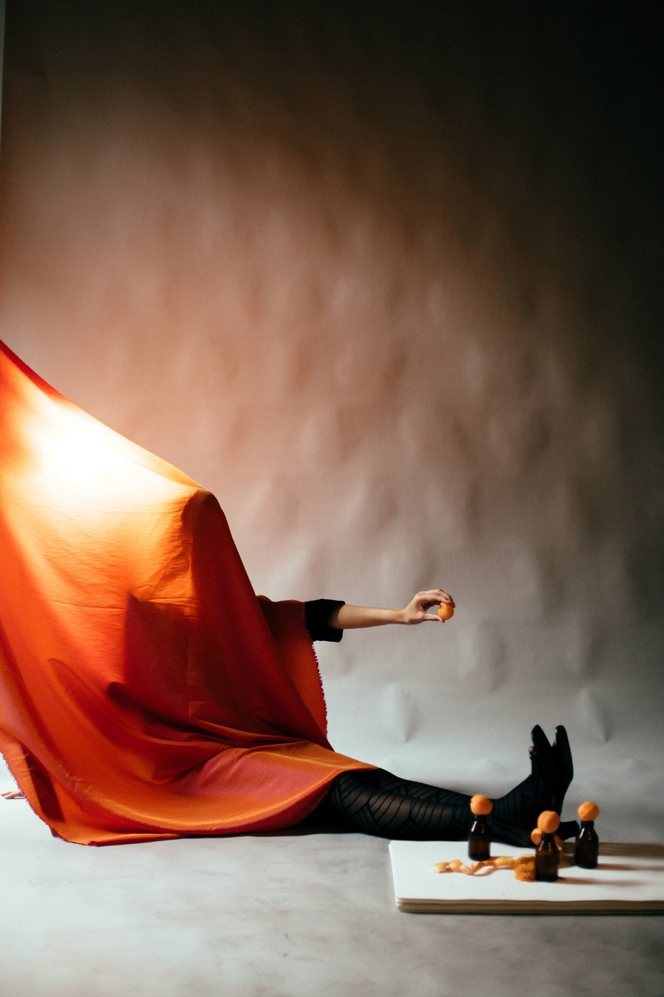 Figure covered in orange fabric, holding a small fruit